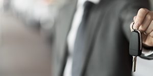 A dealership salesman holds out the keys to a used vehicle.
